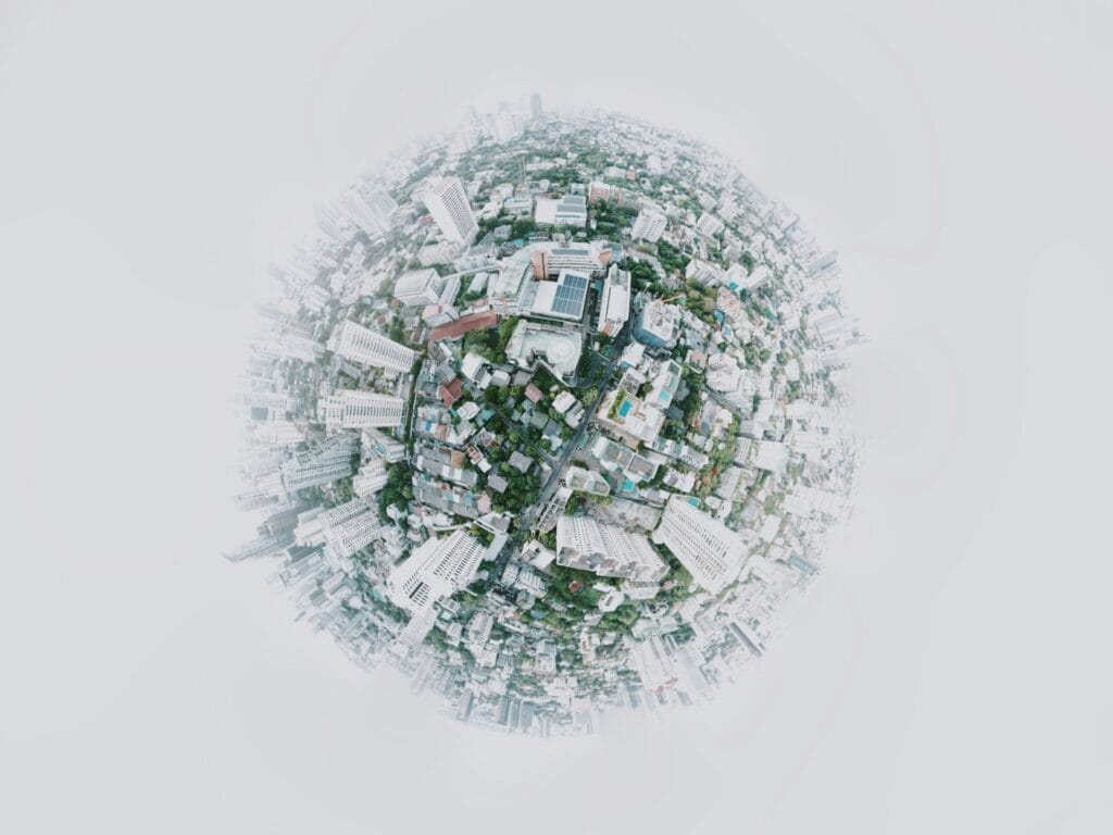 Aerial, circular fisheye view of a densely packed urban city with tall buildings, roads, and greenery, arranged to resemble a tiny planet, surrounded by a white, foggy background that blurs the city edges.